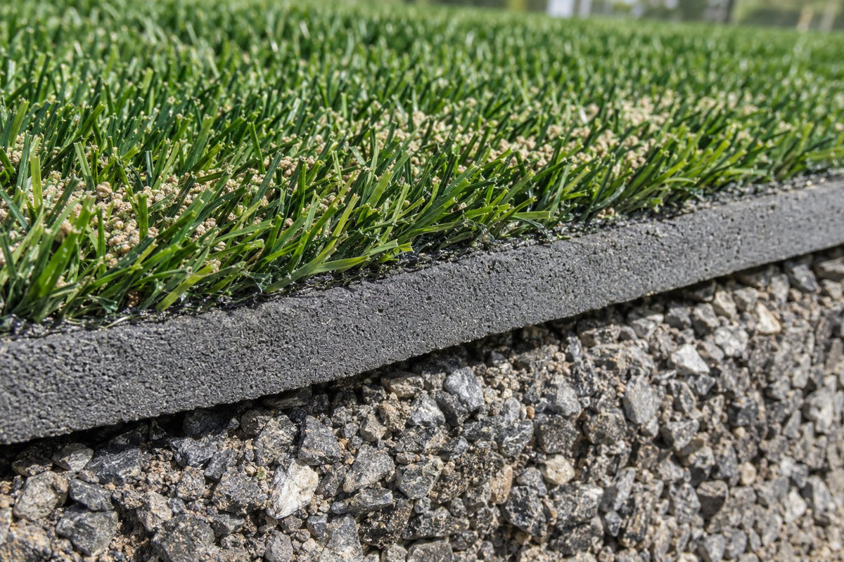 Cutaway of playground turf system: turf fibers and infill over a foam shock pad on a compacted stone base